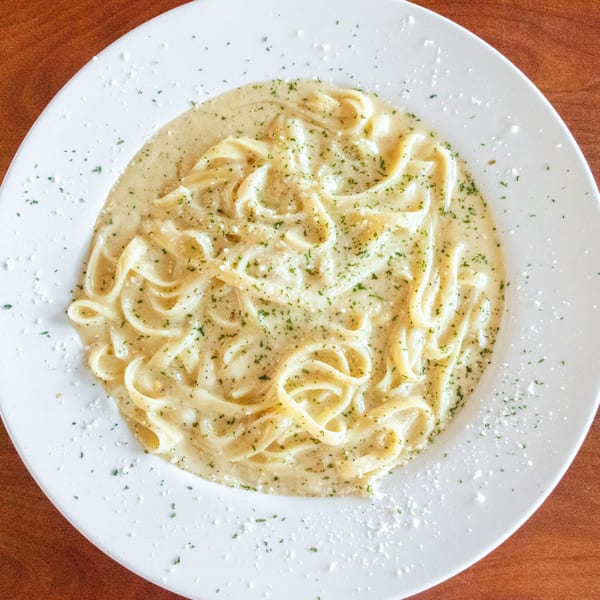 Creamy fettuccine alfredo pasta with parsley and parmesan cheese on a white plate.