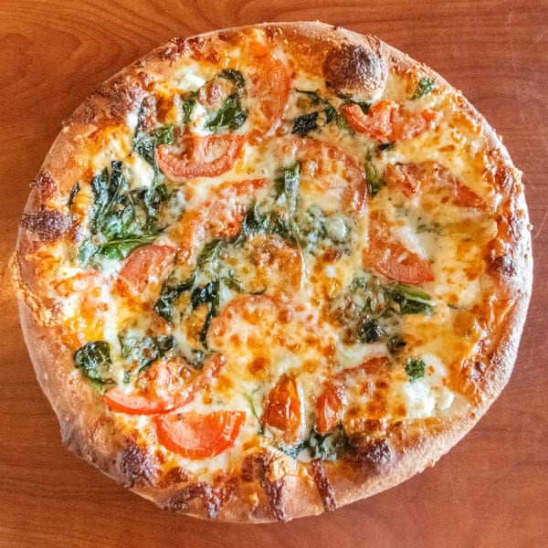 Bella's Pizza Villa's pizza with melted cheese, spinach, and sliced tomatoes on a wooden surface.
