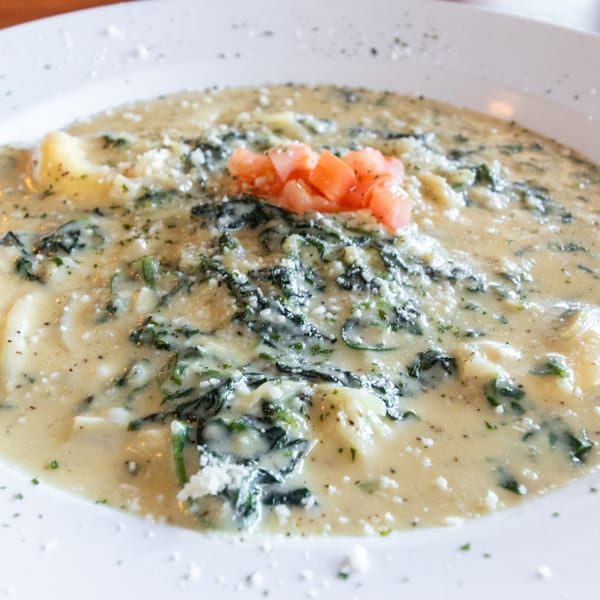 Creamy pasta dish with spinach, parmesan cheese, and diced tomatoes in a white bowl.
