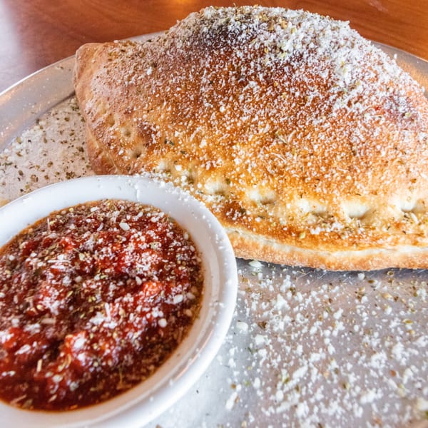 Golden-brown calzone dusted with Parmesan cheese and herbs, served with a side of marinara sauce.