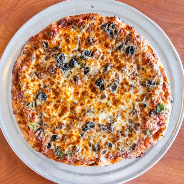 Bella's Pizza Villa's whole baked pizza with melted cheese, black olives, and green peppers on a metal pan.